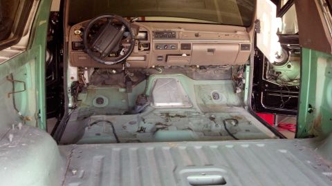 1995 Ford Bronco - The interior of a vehicle is shown stripped down, revealing the bare metal floor and exposed wiring.