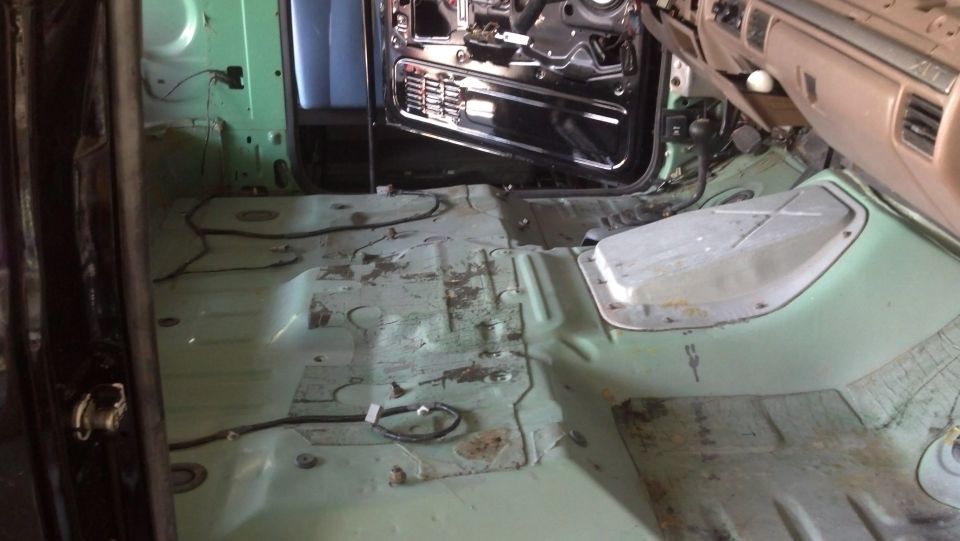 Interior of a vehicle with seats and carpet removed, showing the floor pan and door frame