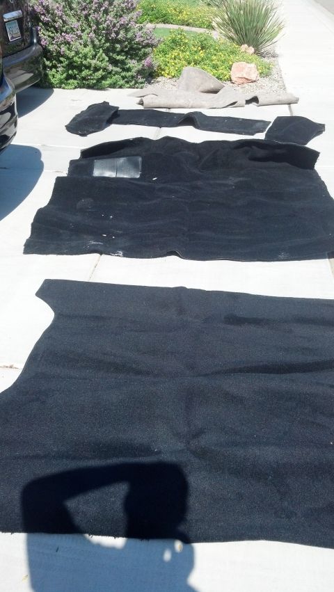 1995 Ford Bronco - Several pieces of black automotive carpet are spread out on a concrete driveway, likely for cleaning or replacement.