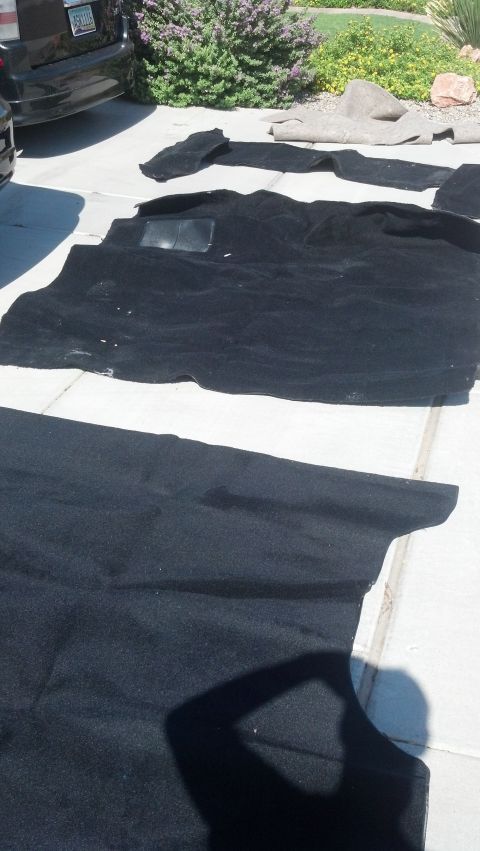 1995 Ford Bronco - Car floor mats are laid out on a concrete surface, with a portion of a dark-colored vehicle visible in the background.