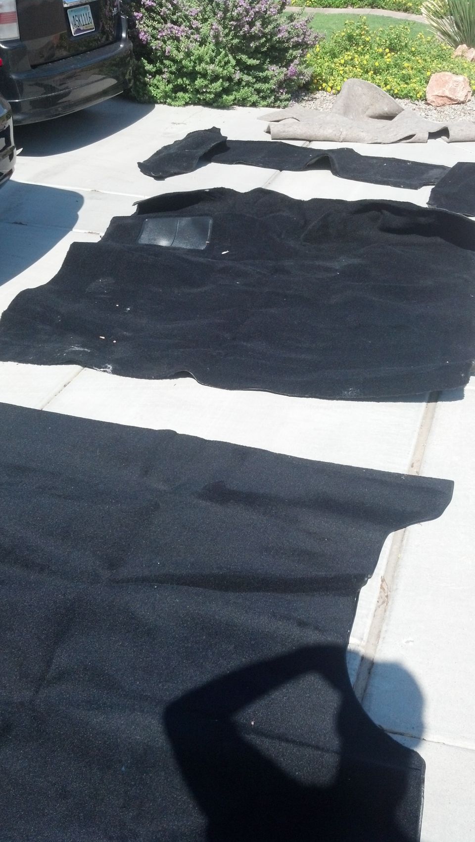 Several black car floor mats laid out on a concrete driveway