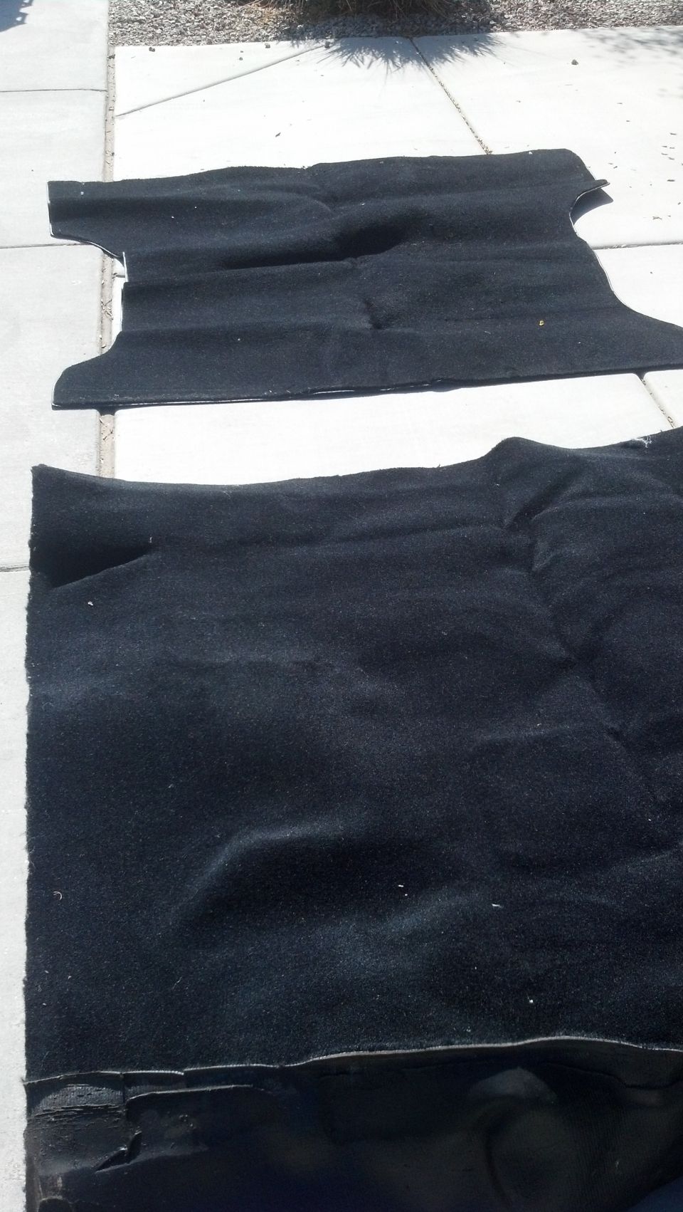 Two black car floor mats laid out on a concrete surface