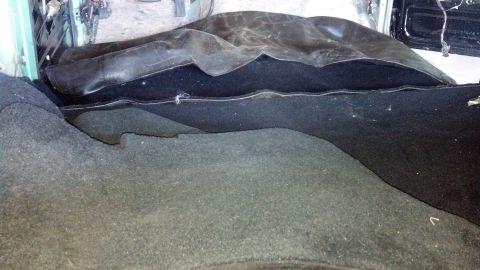 1995 Ford Bronco - The interior of a vehicle shows dark carpeting and a folded black cover, with exposed wires in the background.
