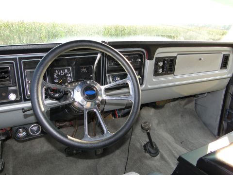 1978 Ford Bronco - The dashboard of a truck shows a custom steering wheel, aftermarket gauges, and a floor-mounted shifter.