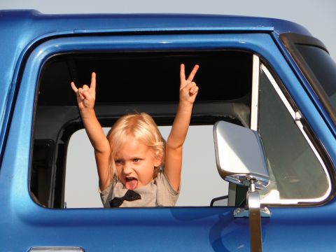 1978 Ford Bronco - A child with blonde hair sticks their tongue out and makes rock on and peace signs from the window of a blue 1978 Ford Bronco.