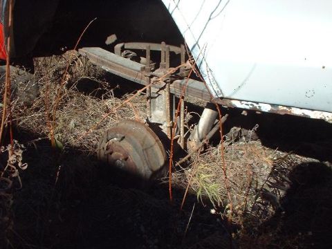 1993 Ford Bronco - Overgrown rear axle components of a vehicle, including a leaf spring and brake drum, are visible.