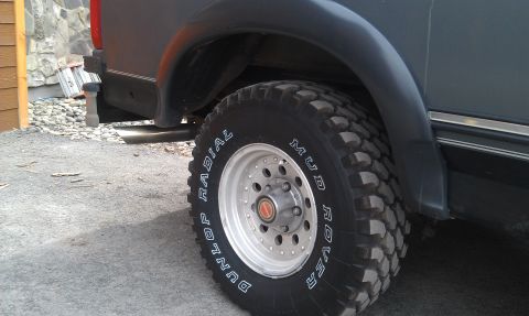 1993 Ford Bronco - Close-up view of the rear wheel and fender flare on a dark SUV, Dunlop Mud Rover tires.