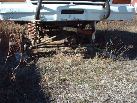 1993 Ford Bronco - Close-up of the front suspension and bumper area of a white vehicle, showing "Hellmaster" shocks and off-road modifications.