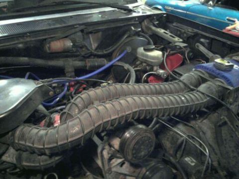 1993 Ford Bronco - Engine bay of a 1993 Ford Bronco shows intake hoses and other components. A blue vehicle is in the background.