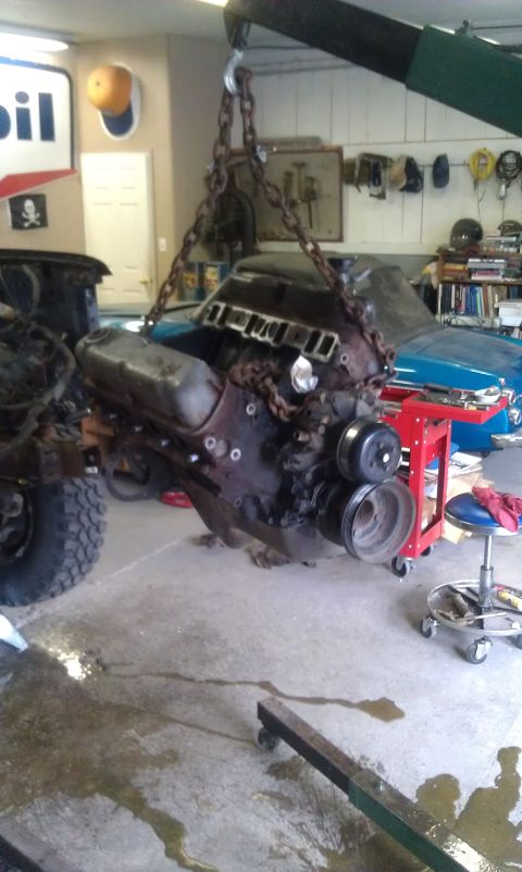 1993 Ford Bronco - An engine is hoisted out of a vehicle in a garage setting, with tools and other car parts visible in the background.