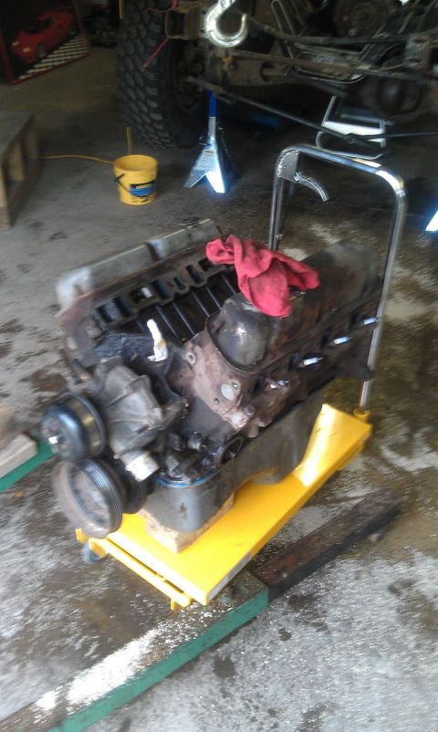 1993 Ford Bronco - Engine removed from a vehicle and placed on a stand for work, with another vehicle in the background.