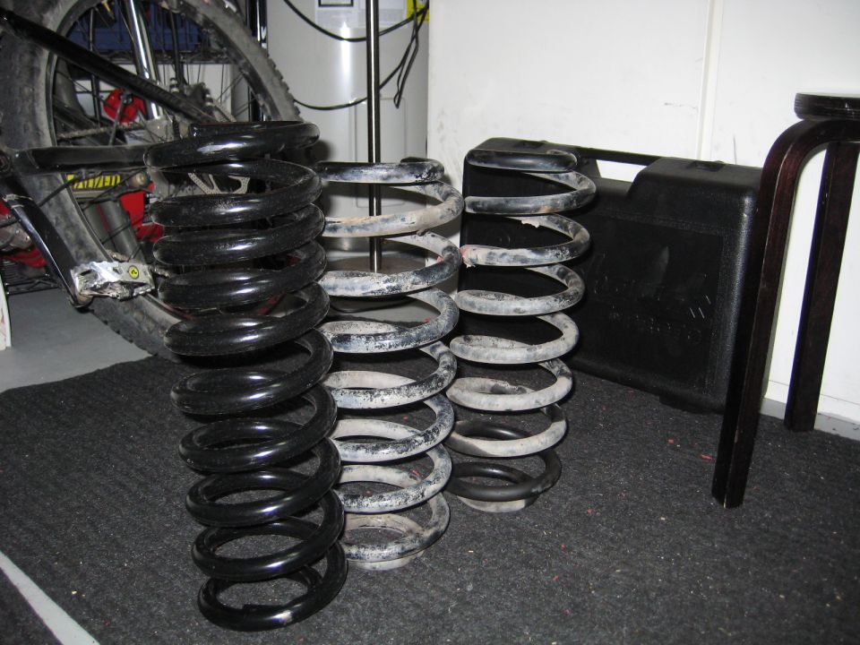 Three stacks of suspension coil springs, one black and two gray, on a carpeted floor