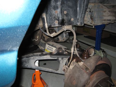 1996 Ford Bronco - Underside shot showing rubber brake lines, an axle, and a rusty brake rotor near a teal painted fender, with an orange jack below.