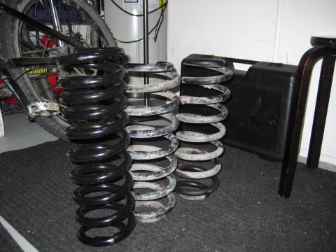 1996 Ford Bronco - A collection of coil springs, including a new black set and two used gray sets, are displayed indoors.