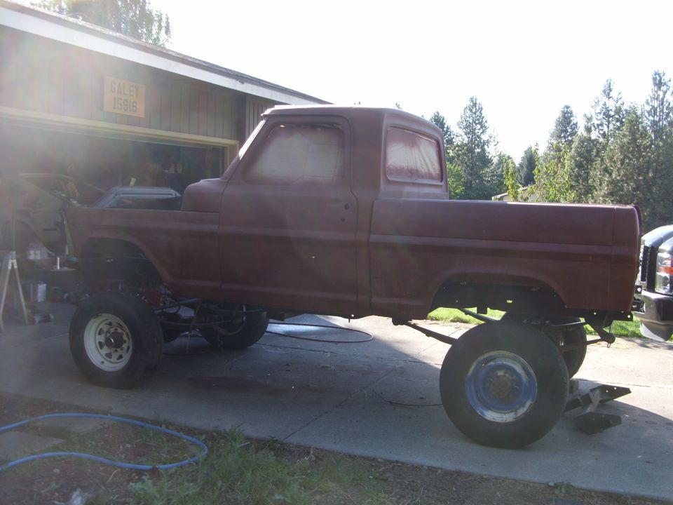 Side view of a maroon 1967 Ford F-250 pickup truck in primer, lifted with large tires