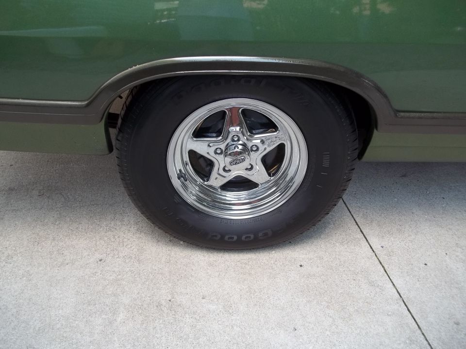 Green vehicle's rear wheel with a chrome star-shaped rim and a 'Goodyear' tire. The fender trim is visible