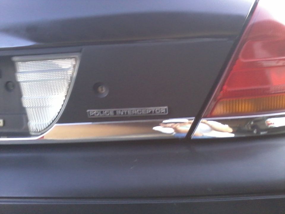 Rear of a dark colored car showing a taillight and a chrome trim piece with a badge that reads 'DODGE INTERCEPTOR'