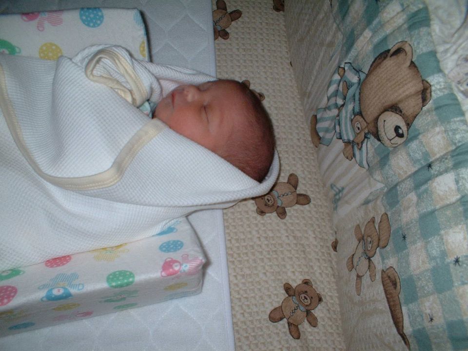 Sleeping swaddled newborn in a crib with teddy bear bedding