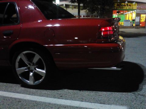 1999 Ford Crown Victoria - Rear view of a red sedan showing its quarter panel and aftermarket wheels.