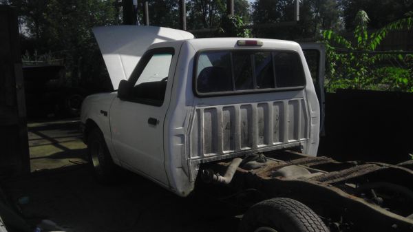 White pickup truck chassis with hood open, rear section removed