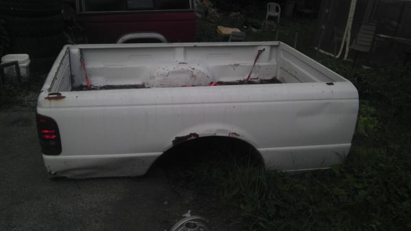 White pickup truck bed with rust around wheel well, seen from the side