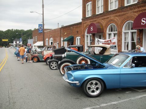 2012 Ford Bronco - A car show features multiple vintage vehicles lined up on a town street, with a blue Mustang prominently displayed.