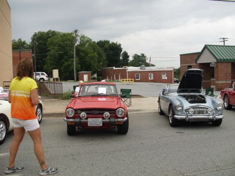 2012 Ford Bronco - A red Triumph TR6 is parked in front of a building, with a silver convertible and other vehicles nearby.