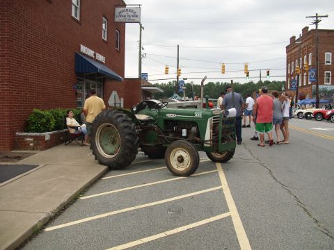 2012 Ford Bronco - A green tractor is parked on the street next to a building, with several people gathered around.