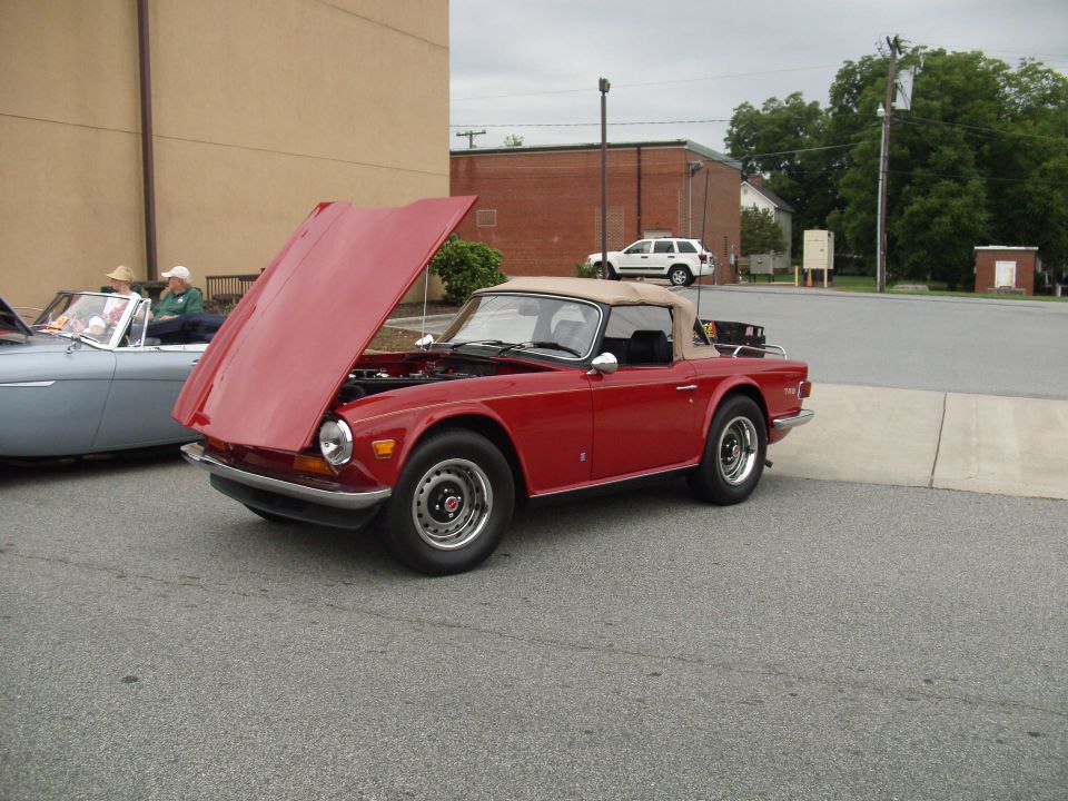 Red convertible sports car with hood open, parked next to a light blue convertible. Another SUV is visible in the background