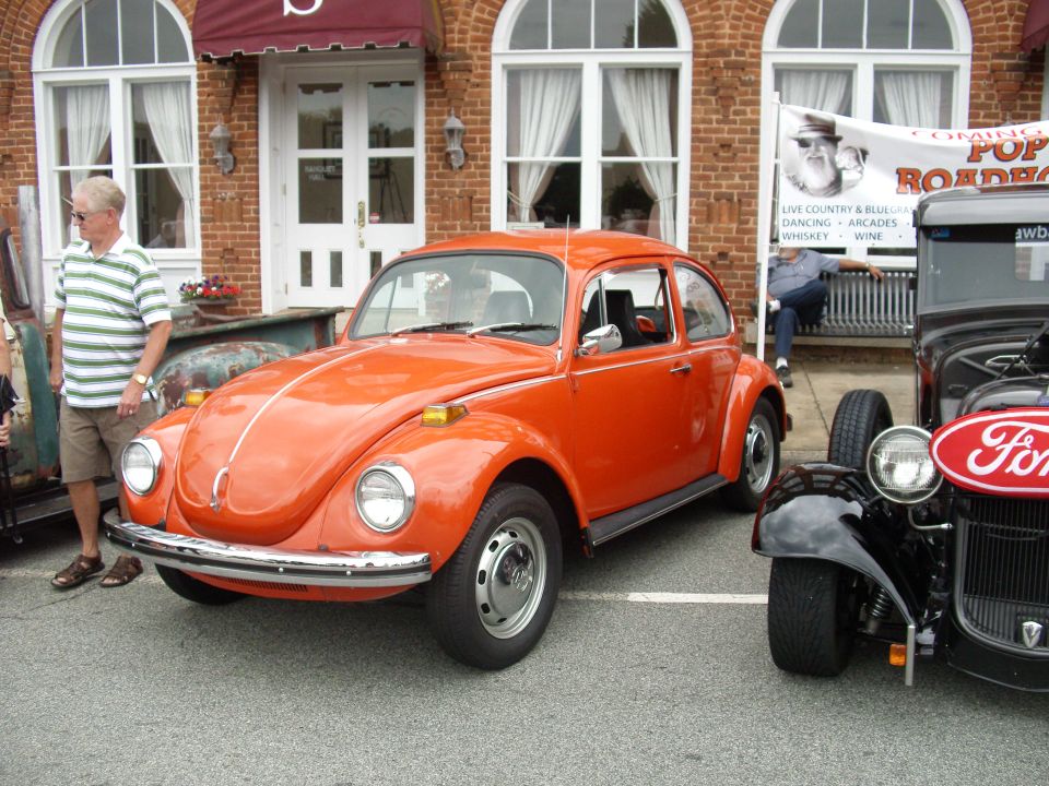 Orange Volkswagen Beetle parked next to a Ford hot rod