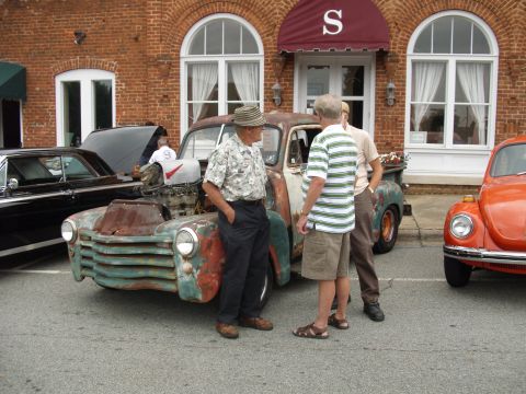 2012 Ford Bronco - A collection of vehicles, including a heavily weathered pickup truck and an orange Volkswagen Beetle, are parked outside a brick building.