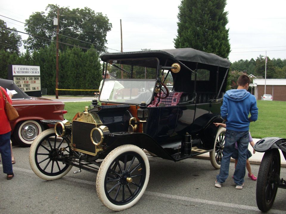 Black antique touring car with white tires and a black soft top, parked next to a red car