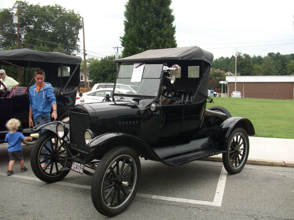 black vintage car with a black soft top, a boy in a blue hoodie stands next to it