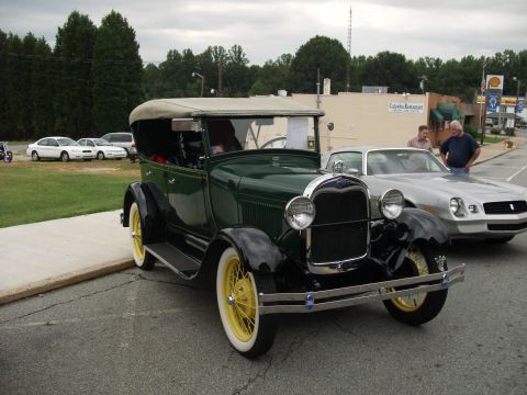 2012 Ford Bronco - An old-fashioned green car with a convertible top is parked on a street next to a modern silver car.
