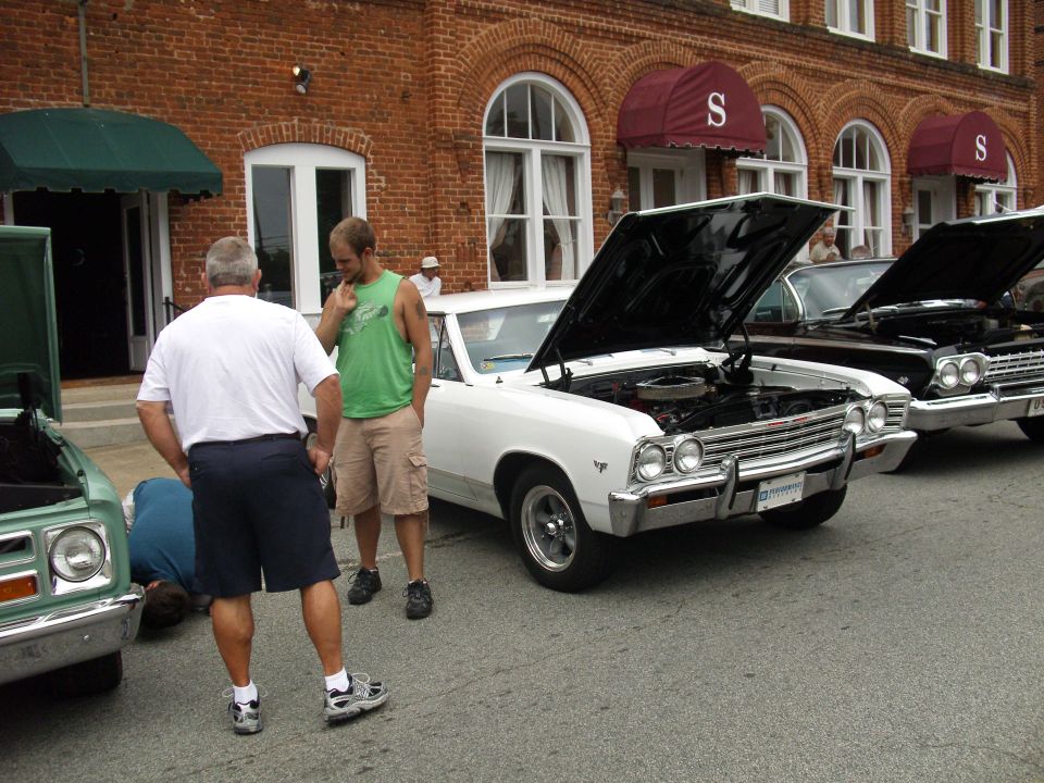White 1966 coupe with hood open, parked on asphalt in front of a brick building