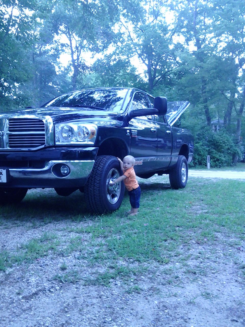 Black Dodge Ram 2500 pickup with toddler hugging front tire on grass