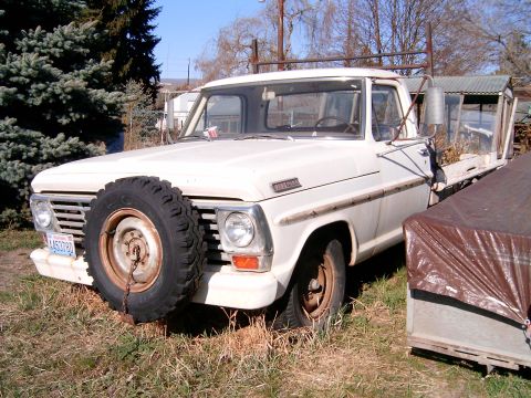 1967 Ford F-250 - A white 1967 Ford F-250 pickup truck sits in a grassy area, a spare tire mounted on its front grille and a flatbed in the rear.
