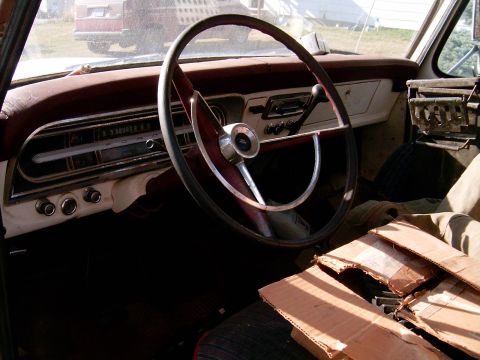 1967 Ford F-250 - The interior of a 1967 Ford F-250 shows its dashboard, steering wheel, and gauges, with another vehicle visible through the windshield.