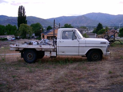 1967 Ford F-250 - A white 1967 Ford F-250 flatbed truck is parked in a dry, grassy field with mountains in the background.