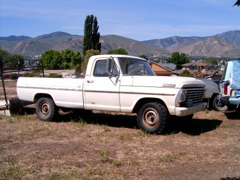 1967 Ford F-250 - A white 1967 Ford F-250 pickup truck is parked in a dry, grassy area with houses and mountains visible in the distance.