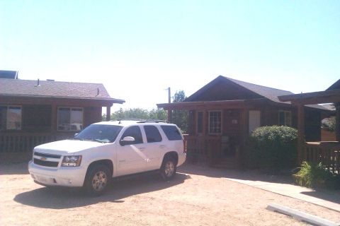 1991 Ford LTD Crown Victoria - A white Chevrolet Tahoe is parked in front of rustic wooden cabins under a clear blue sky.