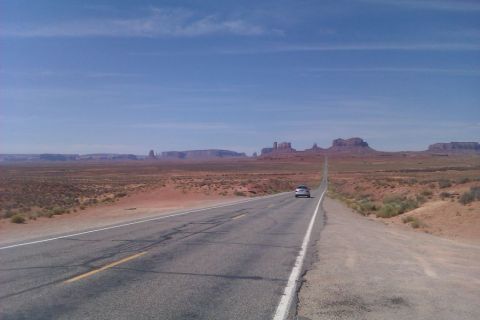 1991 Ford LTD Crown Victoria - A lone car travels down a highway in Monument Valley under a clear blue sky.