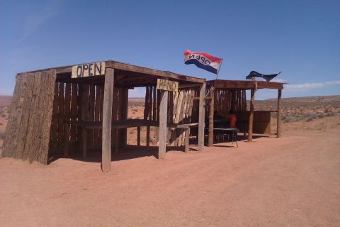 1991 Ford LTD Crown Victoria - Two rustic wooden stalls stand in a dry, desert environment under a clear blue sky.