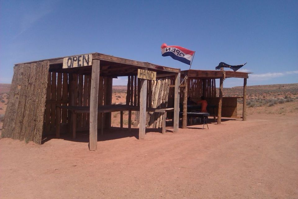 Wooden stalls with 'OPEN' and 'HAND' signs, a red, white, and blue flag, in a desert landscape