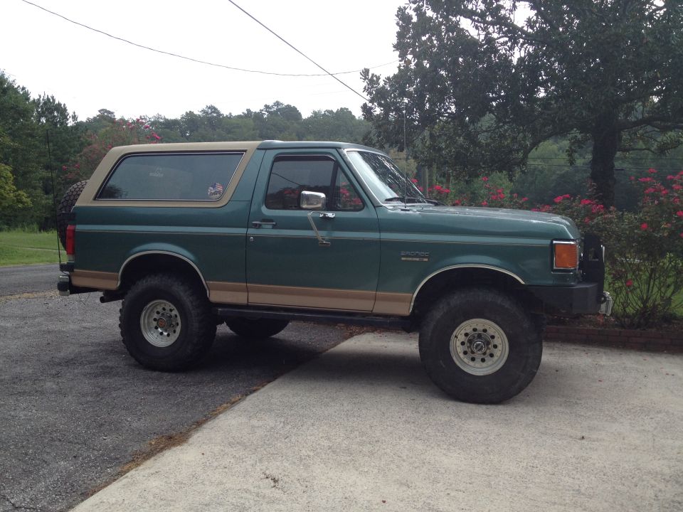 Green Ford Bronco with tan trim and aftermarket wheels parked on a driveway