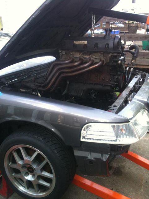 2004 Ford Crown Victoria - Engine installation in progress with the hood open and the engine suspended by a hoist.