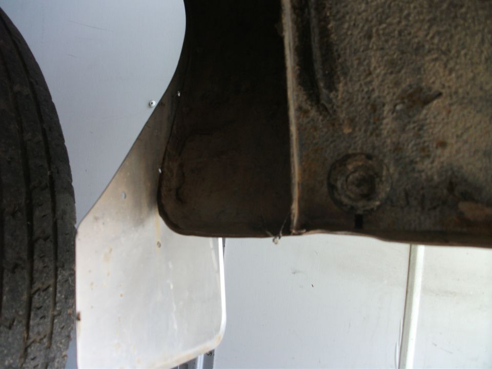 Rusty underbody frame section with bolt, metal panel, and tire at left