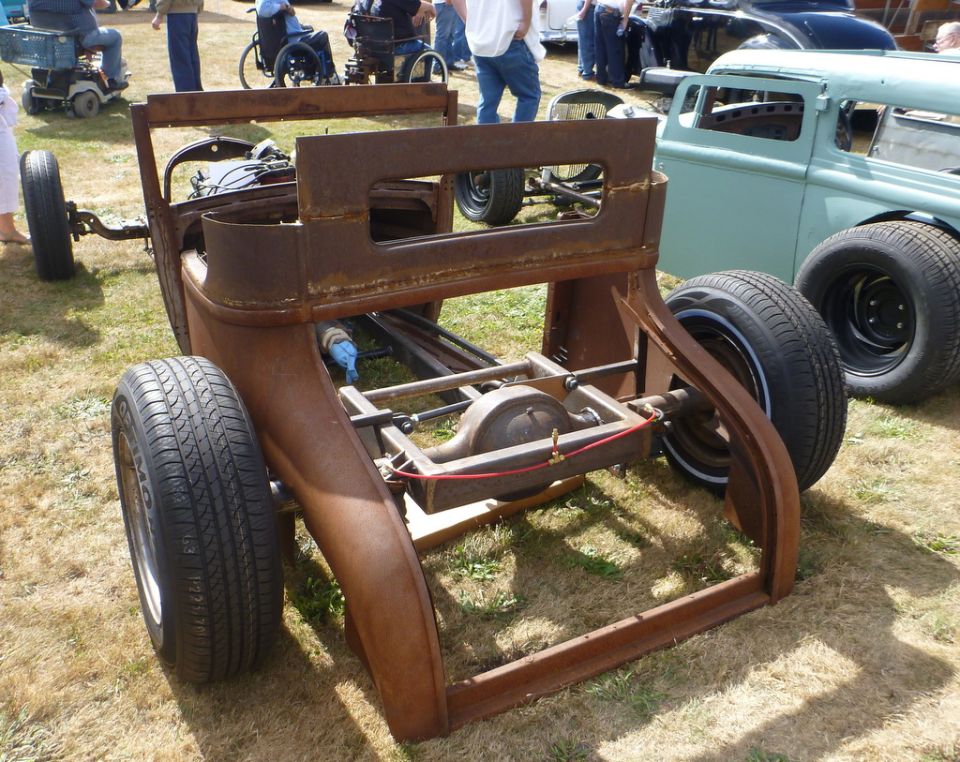 Rusted car chassis, rear view, with other vehicles in background