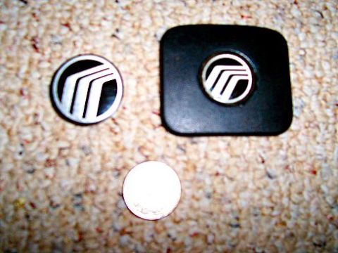 2003 Ford Expedition - Two Mercury emblems, one round and one on a black square part, are shown next to a coin.