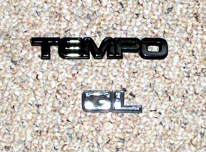 2003 Ford Expedition - Two car emblems, 'TEMPO' and 'GL', are shown on a carpeted surface.